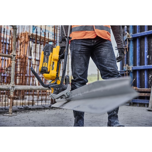 A person wearing construction gear uses a DEWALT cordless metal cutting saw to cut a metal beam at a construction site.