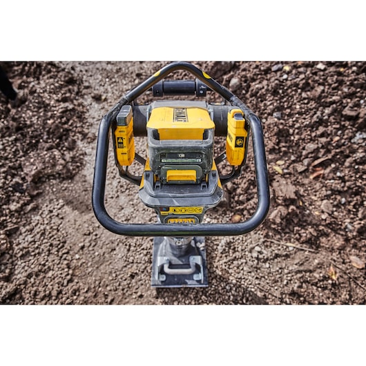 A DEWALT battery-powered compactor standing on a gravel surface outdoors, shown from above with visible handle and control panel.