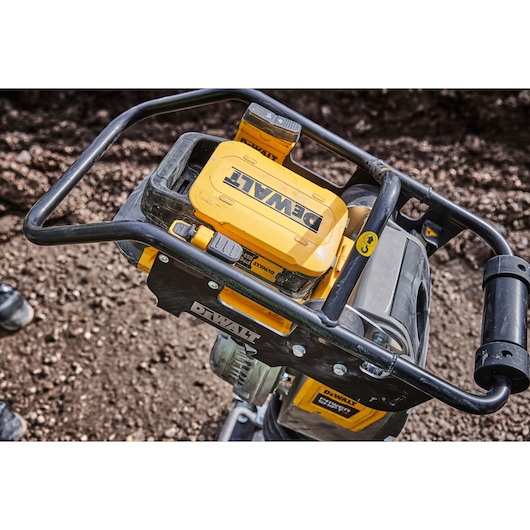 Close-up view of a DEWALT power tool with a yellow and black design, placed on soil. The handle and control panel are visible, and the DEWALT logo is prominently displayed on the top section.