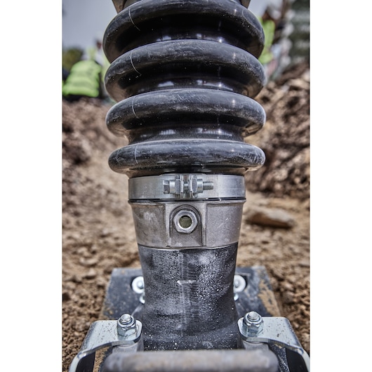 Close-up view of a DEWALT power tool component with a coiled spring and metal fittings, positioned on a construction site with soil in the background.
