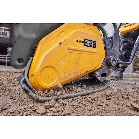Close-up of a DEWALT Power Shift machine in use on a construction site, compacting soil with its yellow base.