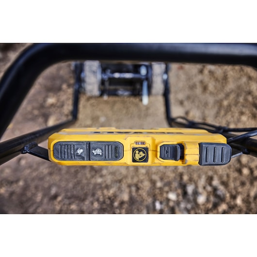 Close-up view of the DEWALT DCPS7154N tool control panel with several black buttons and symbols, mounted on a yellow frame, on an outdoor construction surface.