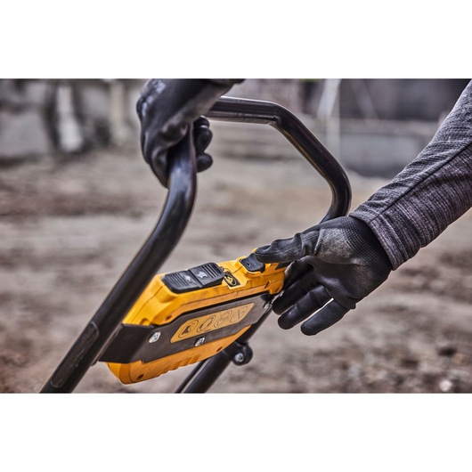 Close-up of gloved hands operating the control panel on a DEWALT outdoor power tool, with a yellow casing and black handle.