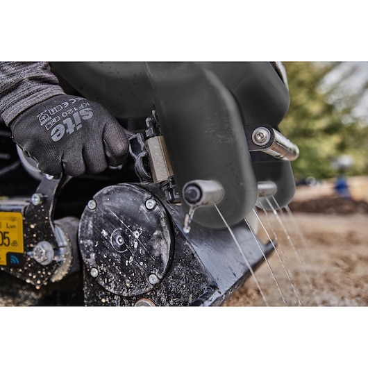 Close-up of a gloved hand operating a DEWALT outdoor machine, with water spraying from multiple nozzles on the equipment.