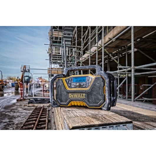 A DEWALT portable radio is placed on a stack of wooden planks at a construction site, surrounded by scaffolding and