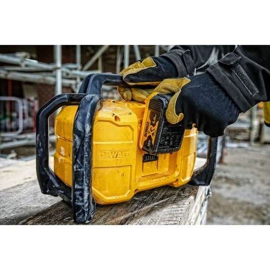 A close-up view of a DEWALT portable radio with a battery being inserted by a person wearing work gloves. The radio is