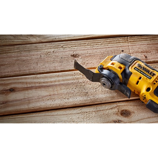 A DEWALT cordless oscillating multi-tool is shown cutting into wooden planks, creating sawdust on the surface.