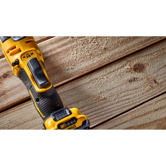 Close-up of a DEWALT cordless power tool resting on a wooden surface with sawdust scattered around.