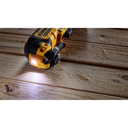 A yellow and black DEWALT power tool with a built-in LED light, positioned on a wooden surface with sawdust.