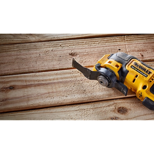A DEWALT cordless oscillating multi-tool is shown in use on wooden planks, creating sawdust.