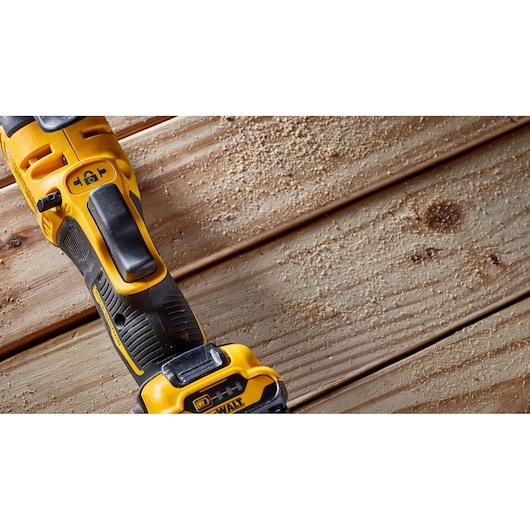A close-up view of a DEWALT cordless power tool on a wooden surface with sawdust.