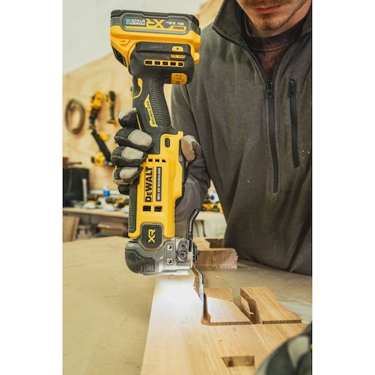 Person using DEWALT cordless jigsaw to cut wood on a workbench in a workshop.
