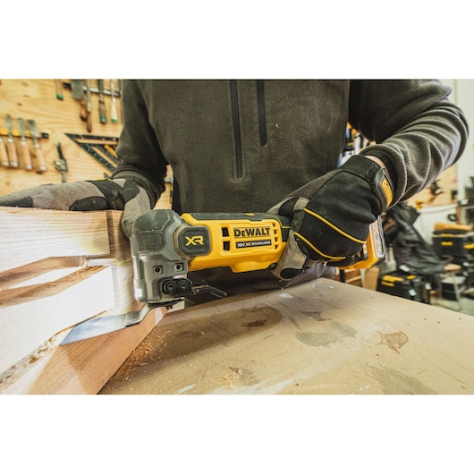 Person using a DEWALT XR brushless power tool to cut wood in a workshop, wearing gloves and workwear.