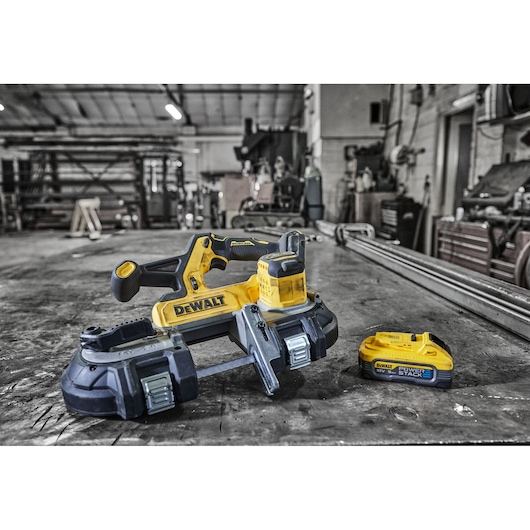 A DEWALT cordless band saw and battery, model DCS378N, placed on a workbench in an industrial workshop setting. The band saw is yellow and black with the DEWALT logo visible, and the battery is also yellow with the label 'POWERSTACK 18V'.