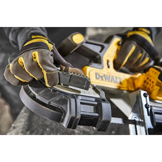 Close-up of gloved hands adjusting a DEWALT cordless band saw tool. The tool features a yellow and black design and is being prepared for use in a workshop setting.