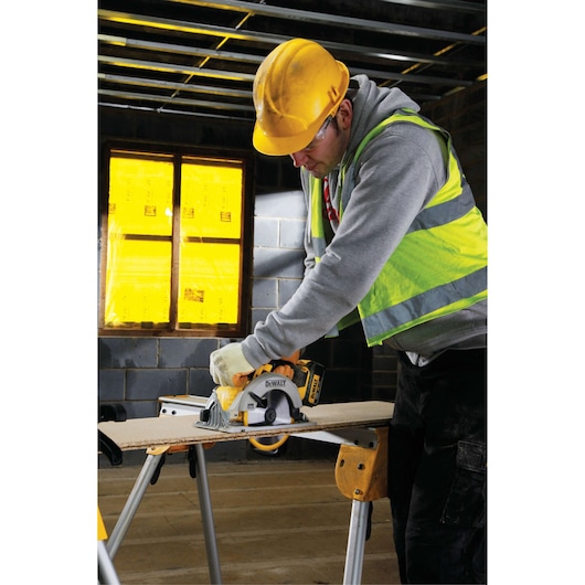 Worker uses a DEWALT circular saw to cut wood on a sawhorse in a construction site.
