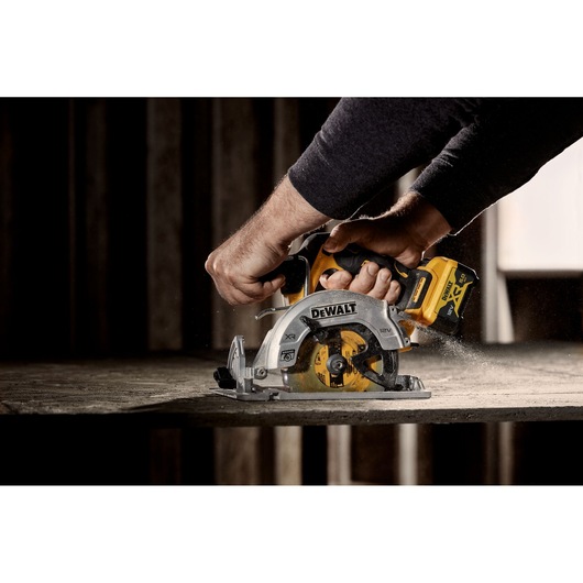 A close-up view of a DEWALT cordless circular saw (DCS512NT) being used to cut through a piece of wood, with sawdust visible.