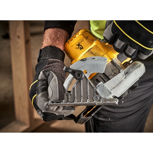 Close-up of gloved hands adjusting the angle settings on a DEWALT DCS565P2 cordless circular saw during woodworking.