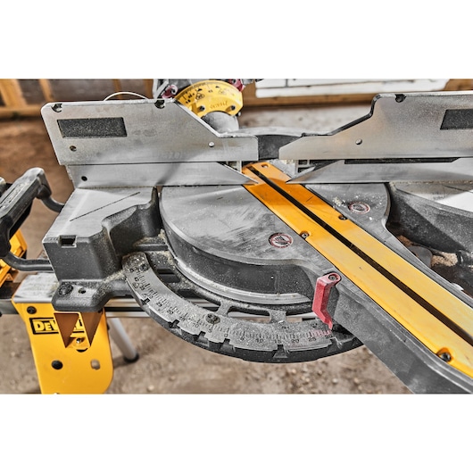 Close-up of a DEWALT miter saw, showing the rotating base with angle markings and a yellow guideline, used for precise cutting of materials on a construction site.