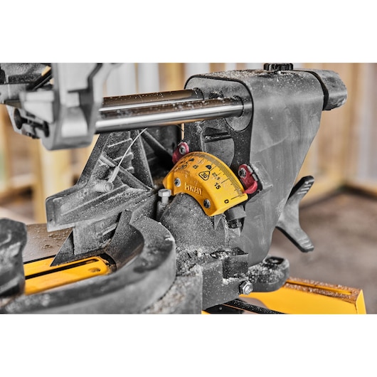 Close-up image of a DEWALT miter saw, showing the angle adjustment gauge and various mechanical components covered in sawdust.