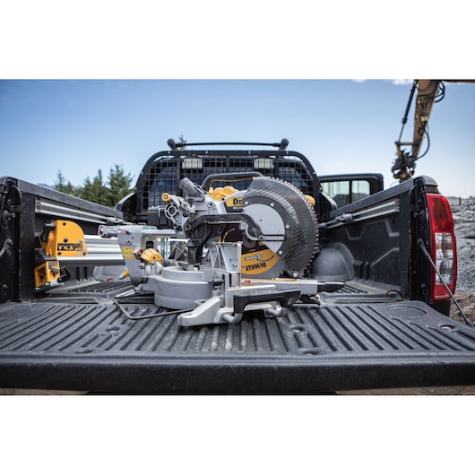 A DEWALT sliding compound miter saw, model DCS782N, is placed in the bed of a black pickup truck outdoors at a construction site.