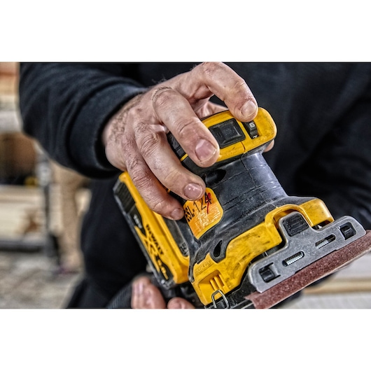 Hand adjusting a DEWALT DCW200NT yellow and black electric sander in a workshop setting.