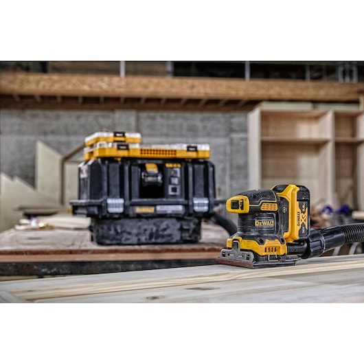 DEWALT DCW200N cordless sander and tool case on a wooden workspace in a workshop.