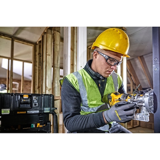 Worker in safety gear uses DEWALT DCW604 tool in a construction setting with wooden frames and equipment visible.