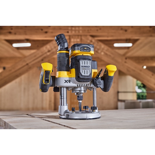 A DEWALT DCW620H2 cordless plunge router with yellow and black accents, placed on a wooden workbench in a workshop setting.