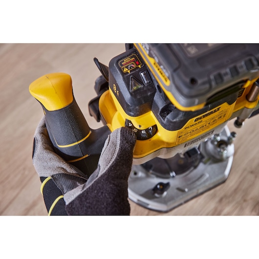 Close-up of a gloved hand adjusting the speed dial on a yellow and black DEWALT power tool, with visible controls and labels, placed on a wooden surface.