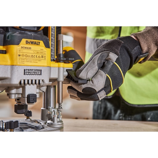 Close-up of a person wearing work gloves adjusting a DEWALT DCW620 power tool on a wooden surface.