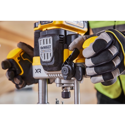 Close-up of gloved hands operating a DEWALT XR brushless power tool, specifically a router, with visible adjustment controls.