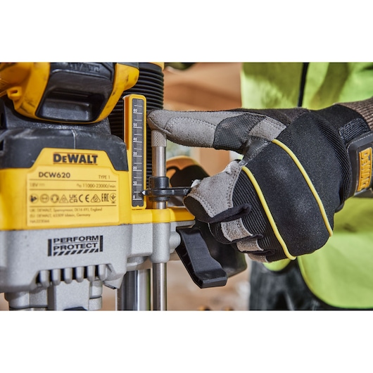 Close-up view of a person wearing protective gloves adjusting the depth setting on a DEWALT DCW620 power tool.