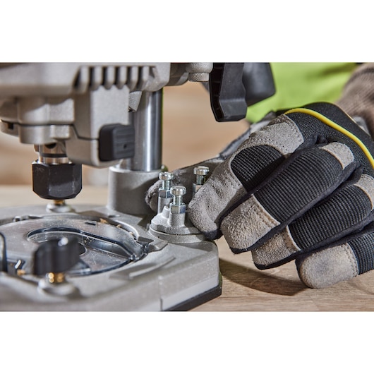 Close-up of a gloved hand adjusting bolts on a DEWALT power tool, positioned on a wooden surface.
