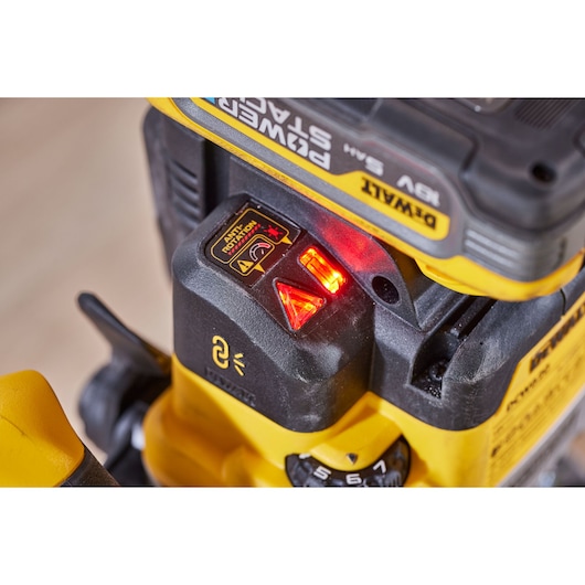 Close-up of a DEWALT DCW620NT power tool, showing illuminated indicator lights and a battery compartment labeled POWER STACK. The control panel displays warning symbols and adjustment settings.