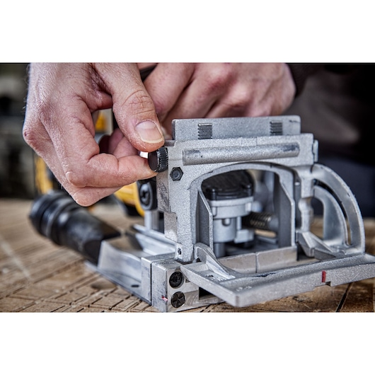 Close-up of a person adjusting a knob on a DEWALT woodworking tool, likely a biscuit joiner, on a wooden surface.