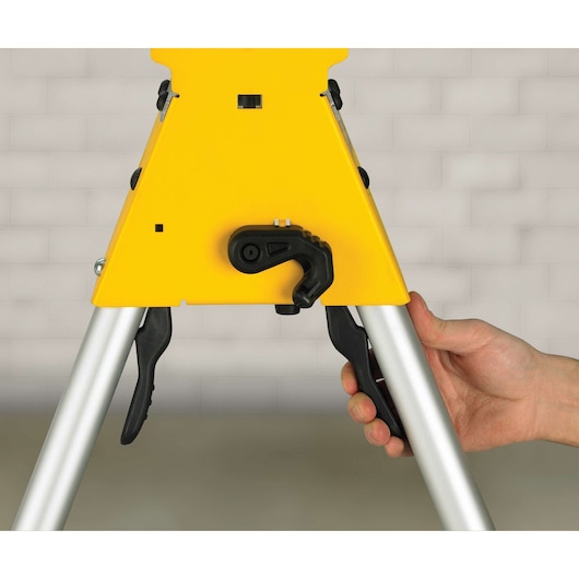 Close-up of a hand adjusting the locking mechanism on a DEWALT DE7033 photography stand with a yellow metal frame and silver legs.