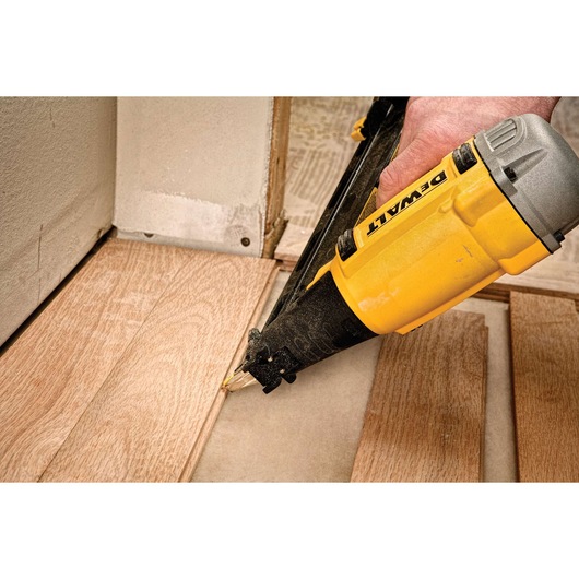 A person using a DEWALT nail gun to install wooden flooring near a wall.