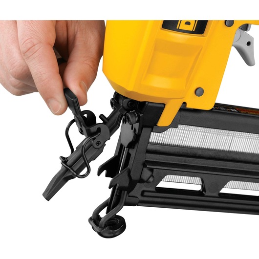 Close-up of a person's hand adjusting the front mechanism of a yellow and black DEWALT nail gun, showing the tool’s detailed parts and loading area.