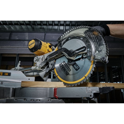 Close-up of a DEWALT miter saw cutting a wooden plank in an industrial setting.