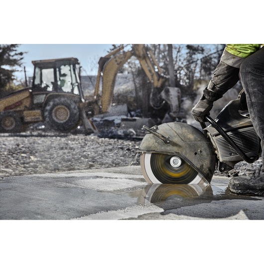 A DEWALT saw with DT20462 blade cuts concrete on a construction site. Heavy machinery is visible in the background.