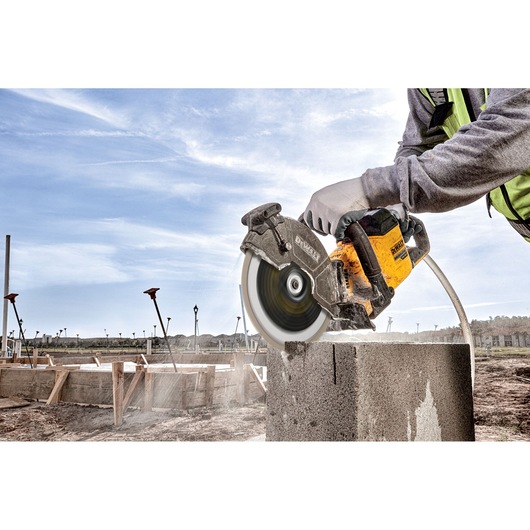 Person cutting concrete block outdoors with DEWALT power saw; dust and debris visible.