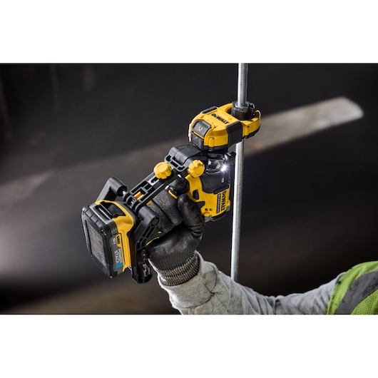 A DEWALT power tool is held by a gloved hand, cutting a metal rod in a dark industrial setting.