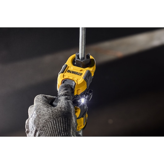 Gloved hand using a DEWALT DT20562 power tool to cut metal rod, tool features LED light.