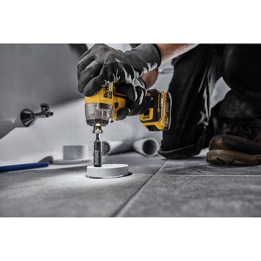 DEWALT DT20563 drill in use, drilling a hole in a tile floor. Worker wears gloves for safety.