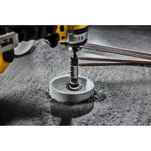 DEWALT drill with hole saw attachment cutting into concrete surface, metal rods visible nearby.