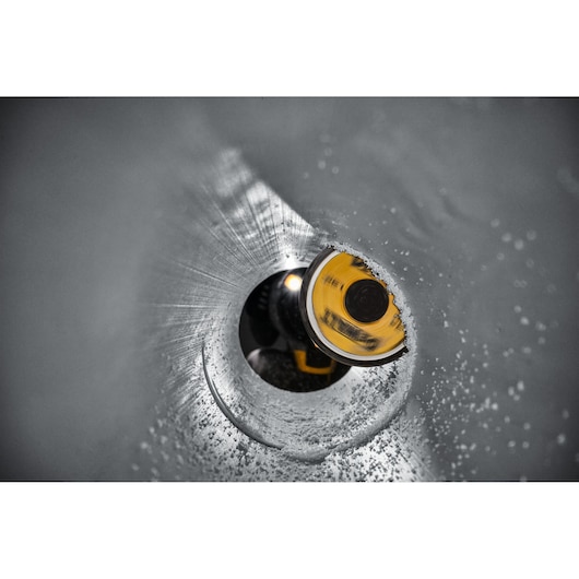 Close-up of a DEWALT yellow hole saw cutting through a metal pipe, surrounded by metal shavings.