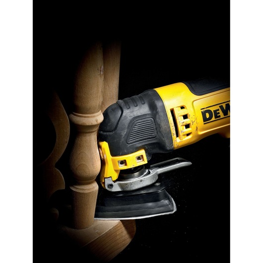 A DEWALT oscillating multi-tool sanding a wooden furniture leg, demonstrating its use for detailed woodworking tasks.