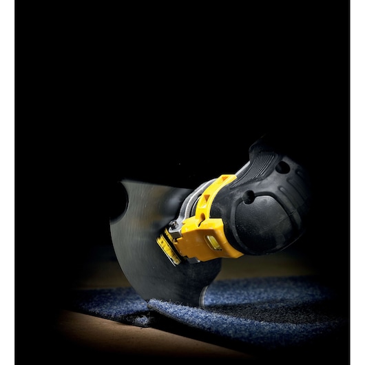 A DEWALT oscillating tool with a cutting blade is being used to cut through blue carpet flooring.