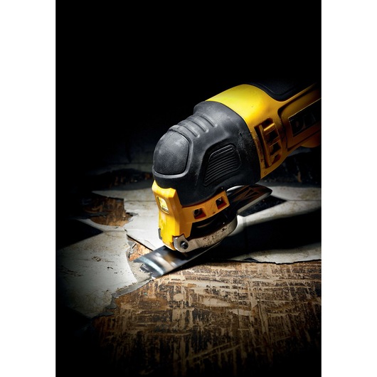 A DEWALT oscillating multi-tool is shown cutting through a piece of flooring. The tool has a yellow and black design with a metal cutting attachment at the front.